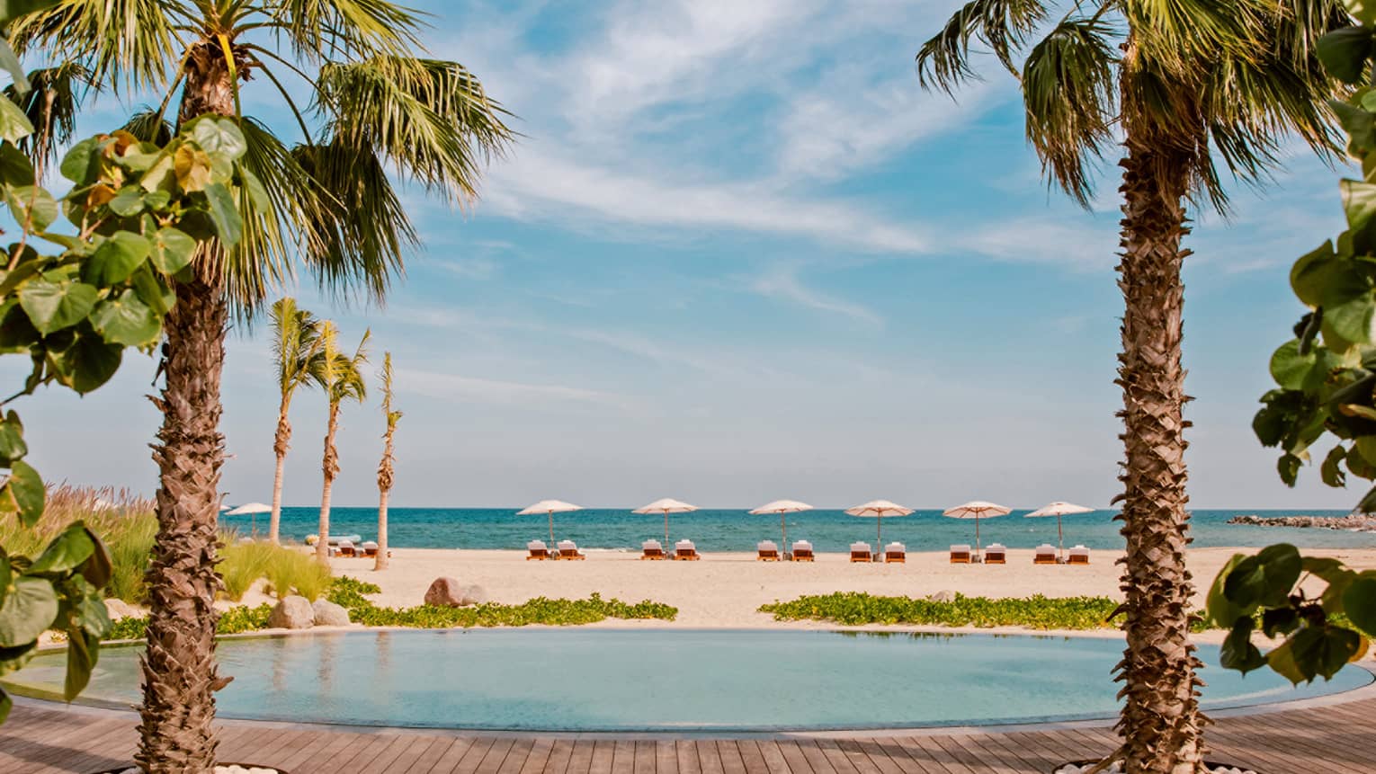 A round pool next to a white sand beach and palm trees.