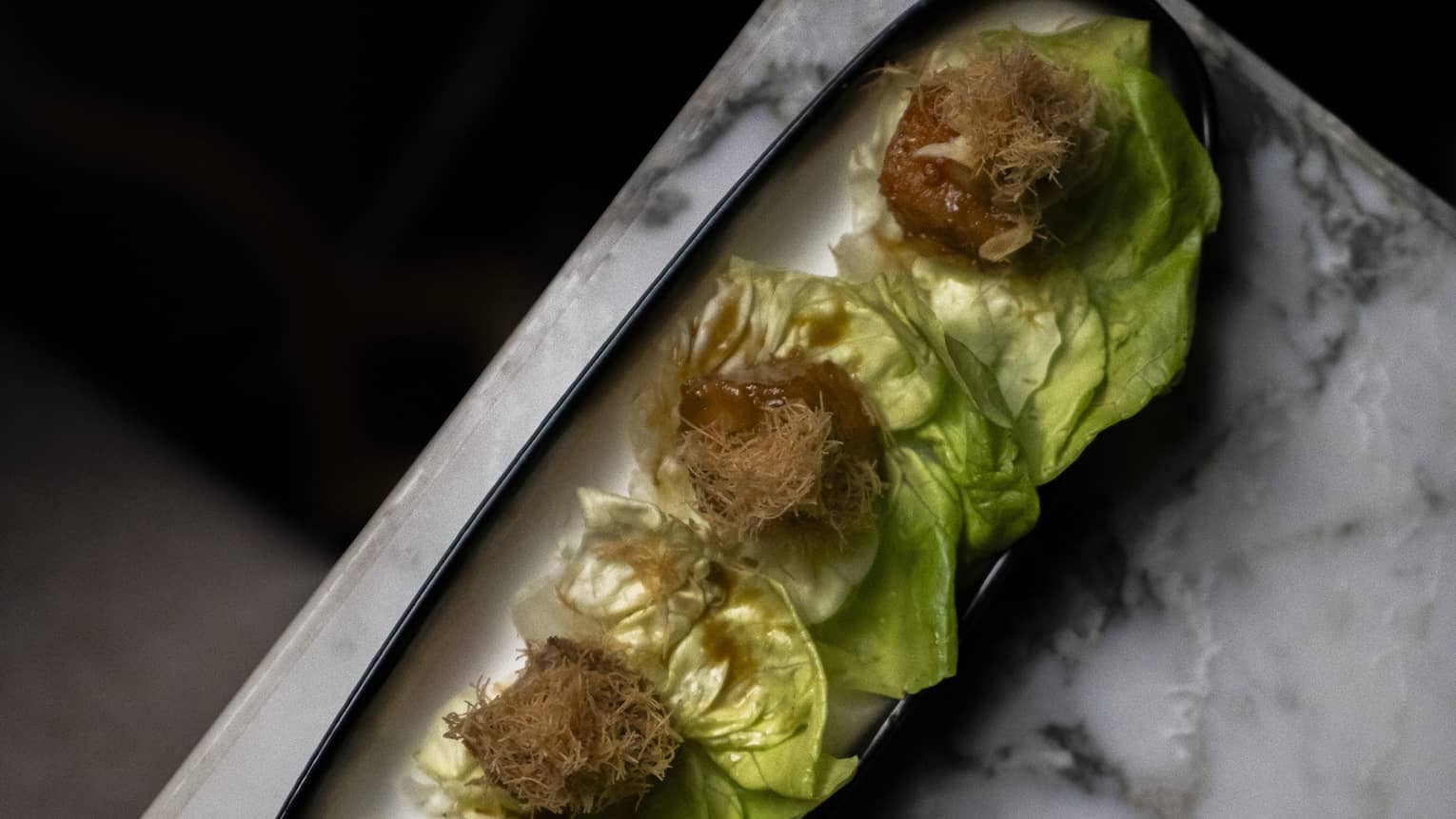 Black cod tapas served with lettuce on a black rectangular platter