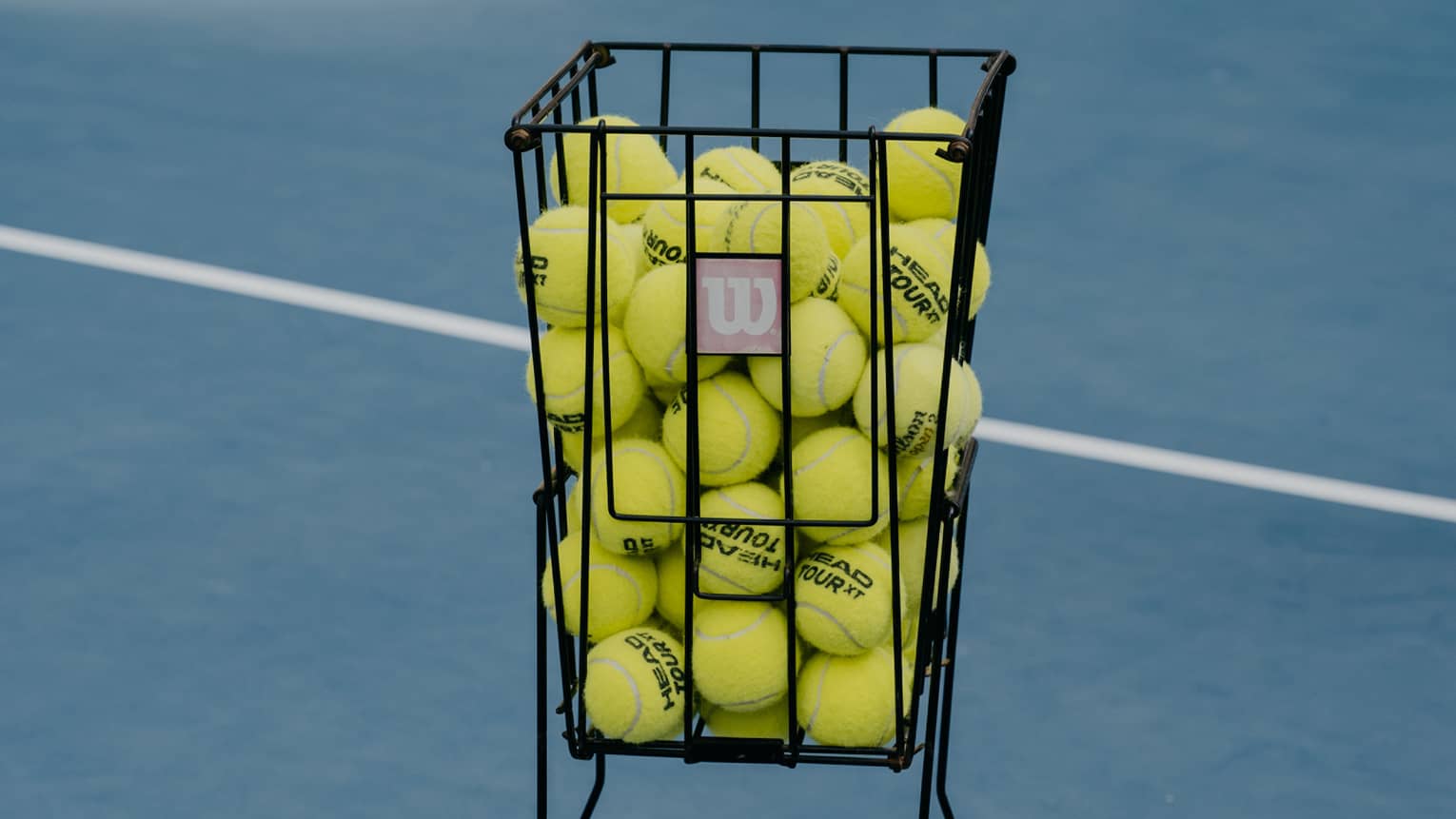 A basket of tennis balls on a blue tennis court