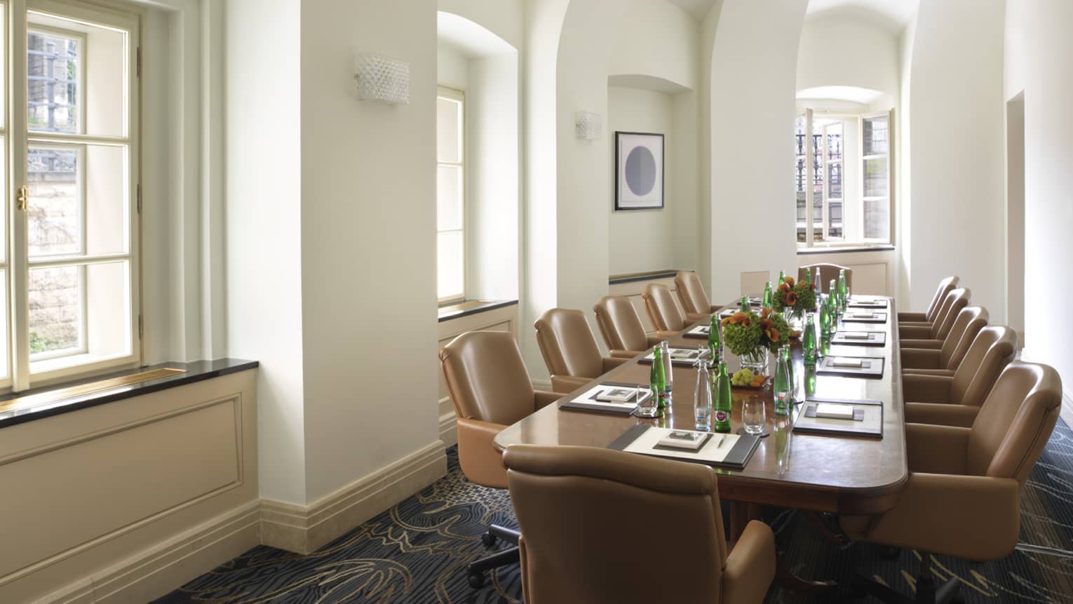 Sunny meeting room with large boardroom table lined with tan executive chairs