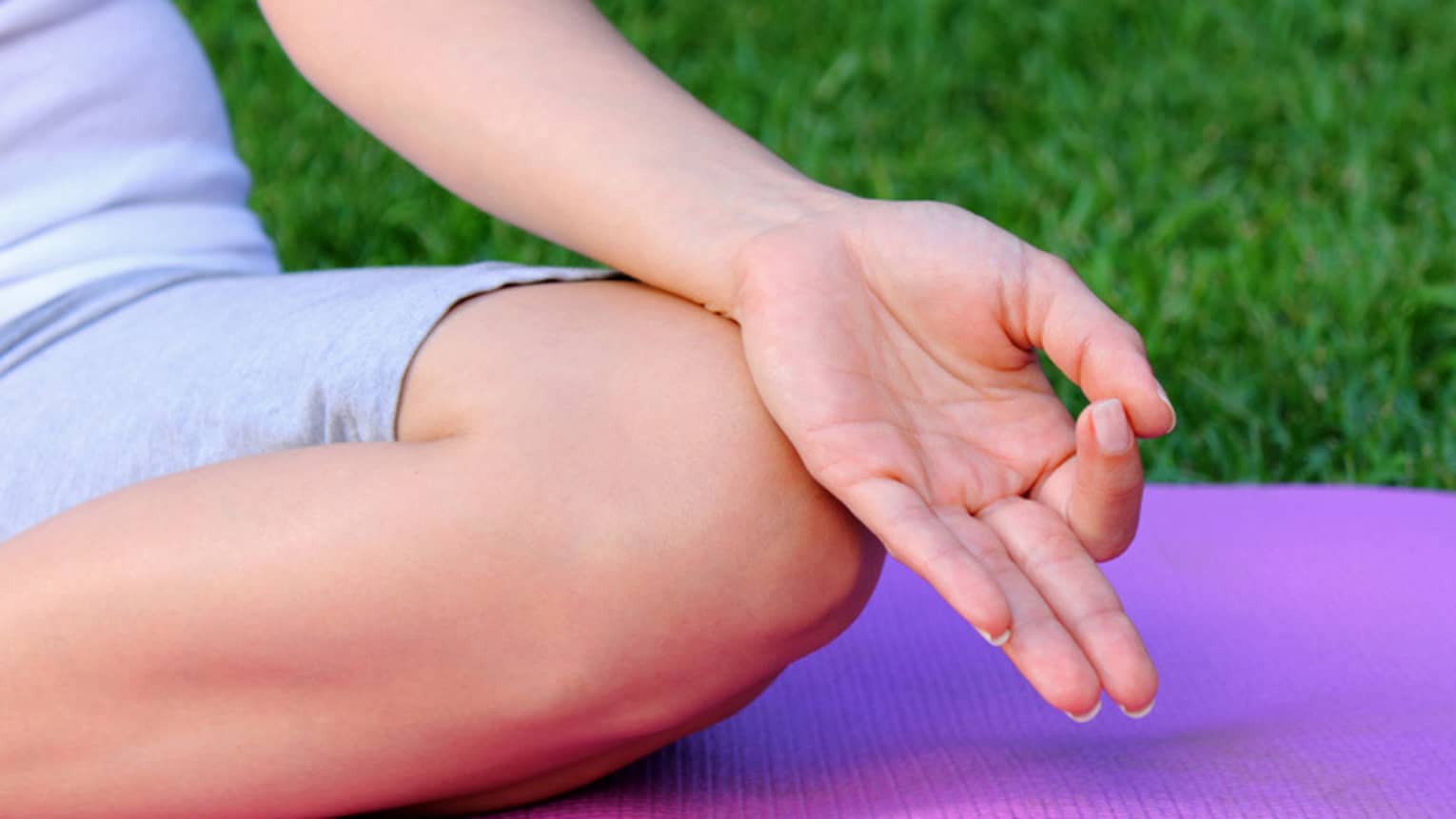 Side of hand, leg in cross legged meditation pose on yoga mat 