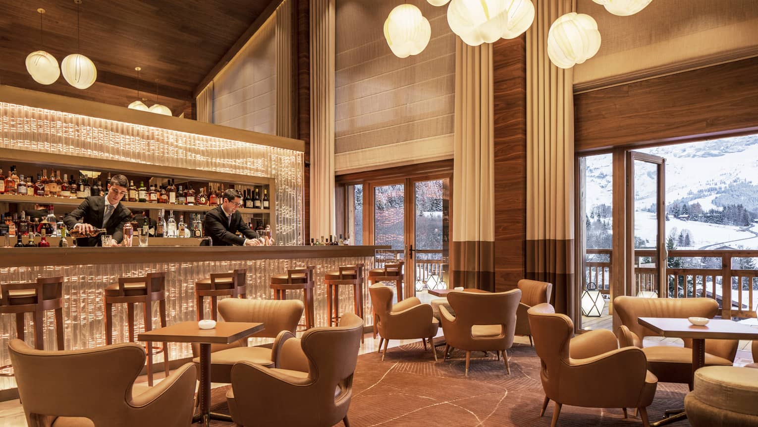 Bartenders mix drinks at Le 1920 bar by midcentury-style lounge chairs, tables, under soaring ceilings