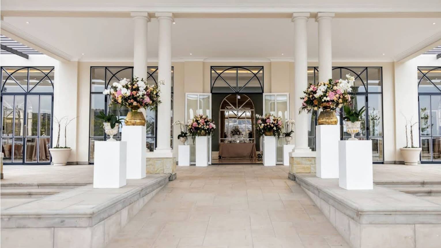An elegant covered entrance to a ballroom space, with stone walkway, plantings and a doorway framed by stately columns.