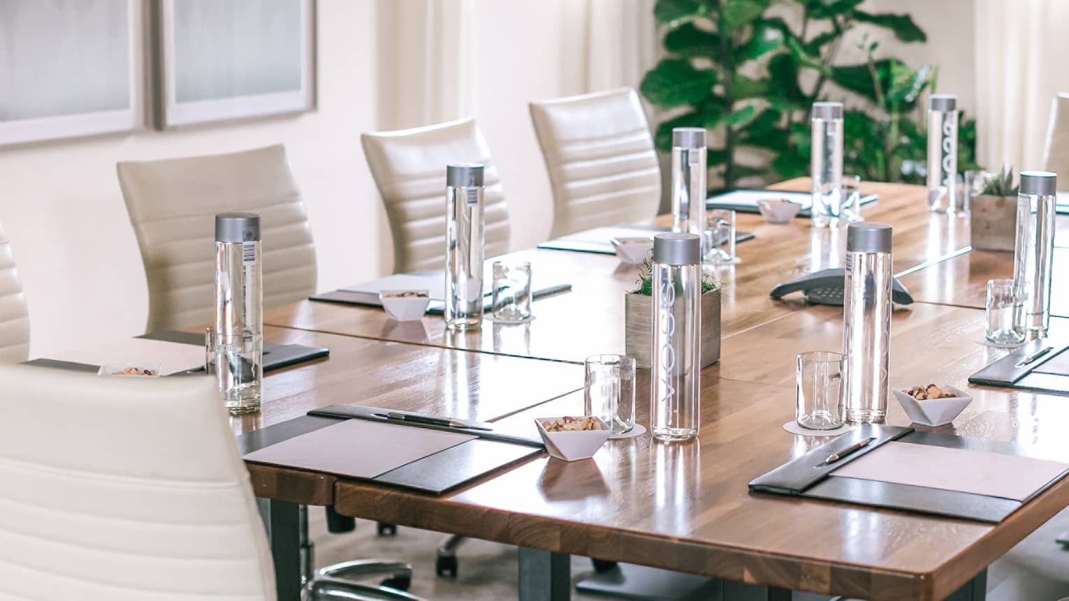 A rectangular boardroom table set with clear glass water bottles and black folders in a naturally-lit room