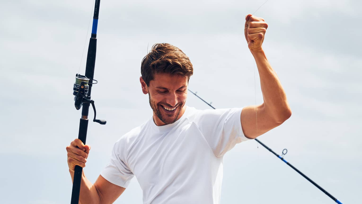 A man near the ocean holding a fishing line with a fish caught on it.