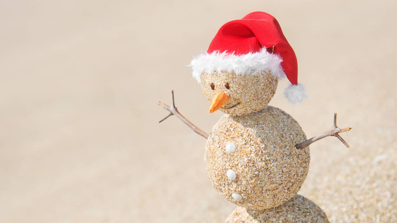 A snowman made out of sand with a red Santa hat.