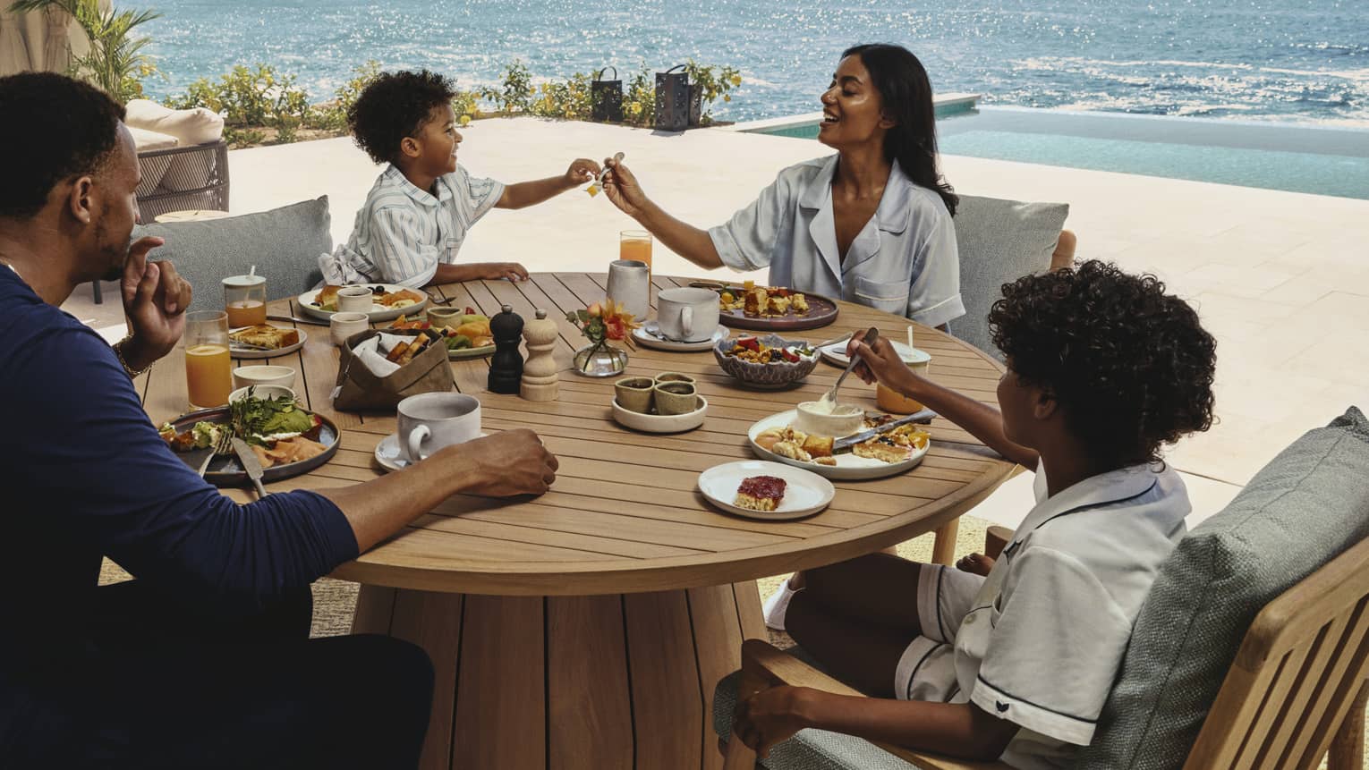Family enjoying breakfast together at a round wooden table on an ocean-view terrace at a luxury resort