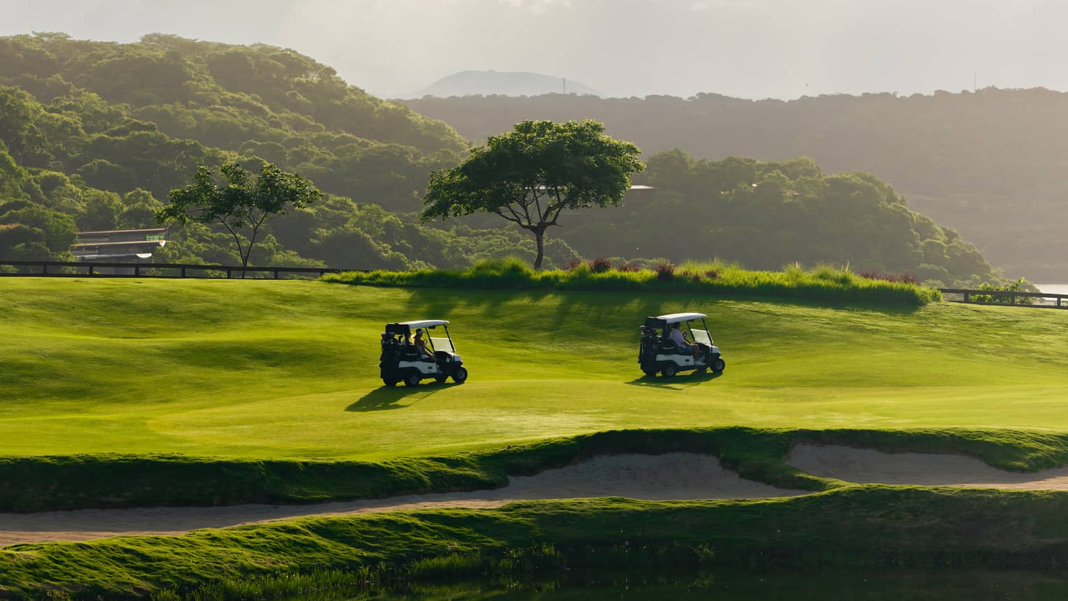 Two golf carts drive along a course next to a water feature