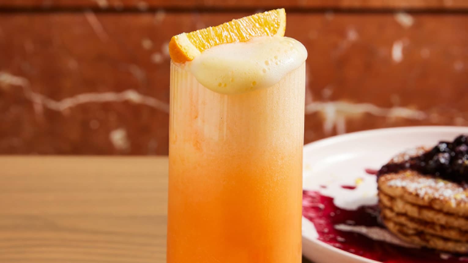 A glass of red and orange drink with an orange slice