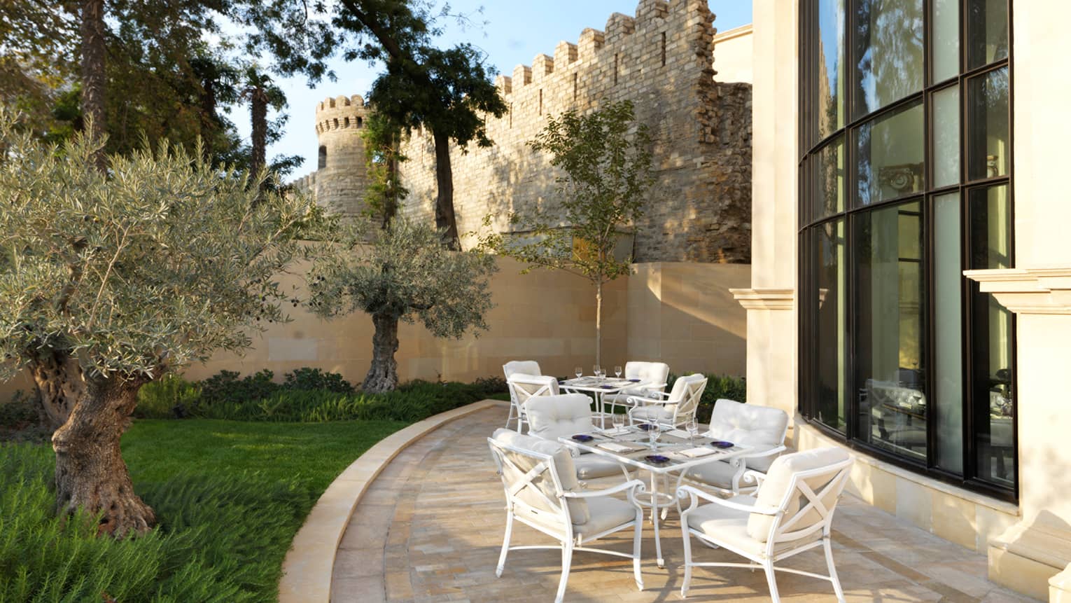 Zafferano curved patio with white iron tables and chairs, historic castle-like wall in background