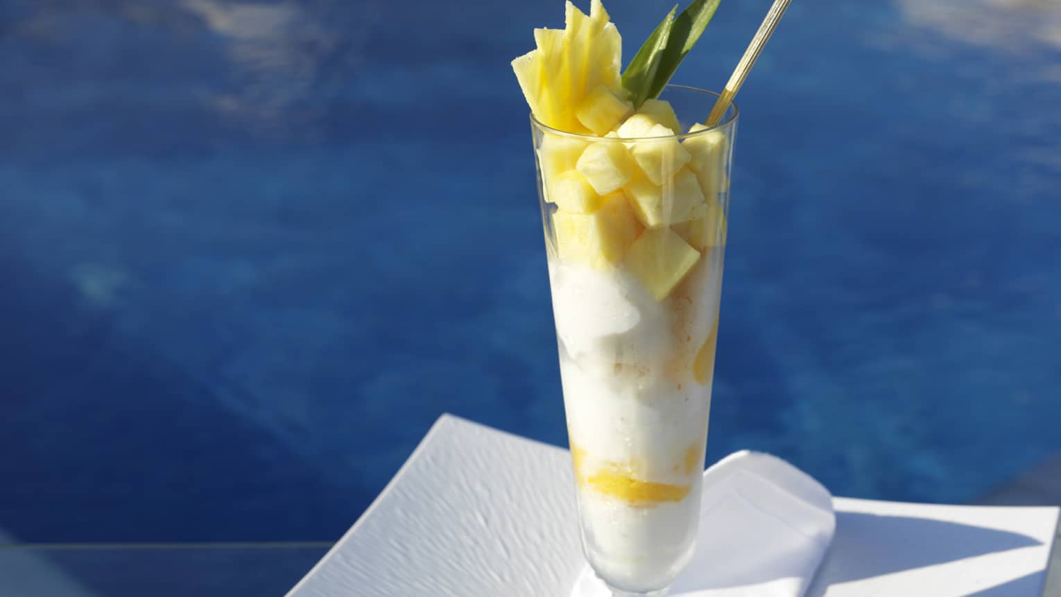 Pineapple and ice cream in tall glass with spoon, set next to a pool