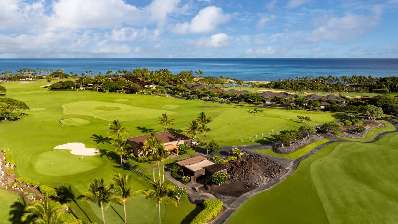 Aeriel view of a lush green golf course with natural lava formations and the ocean in the background.