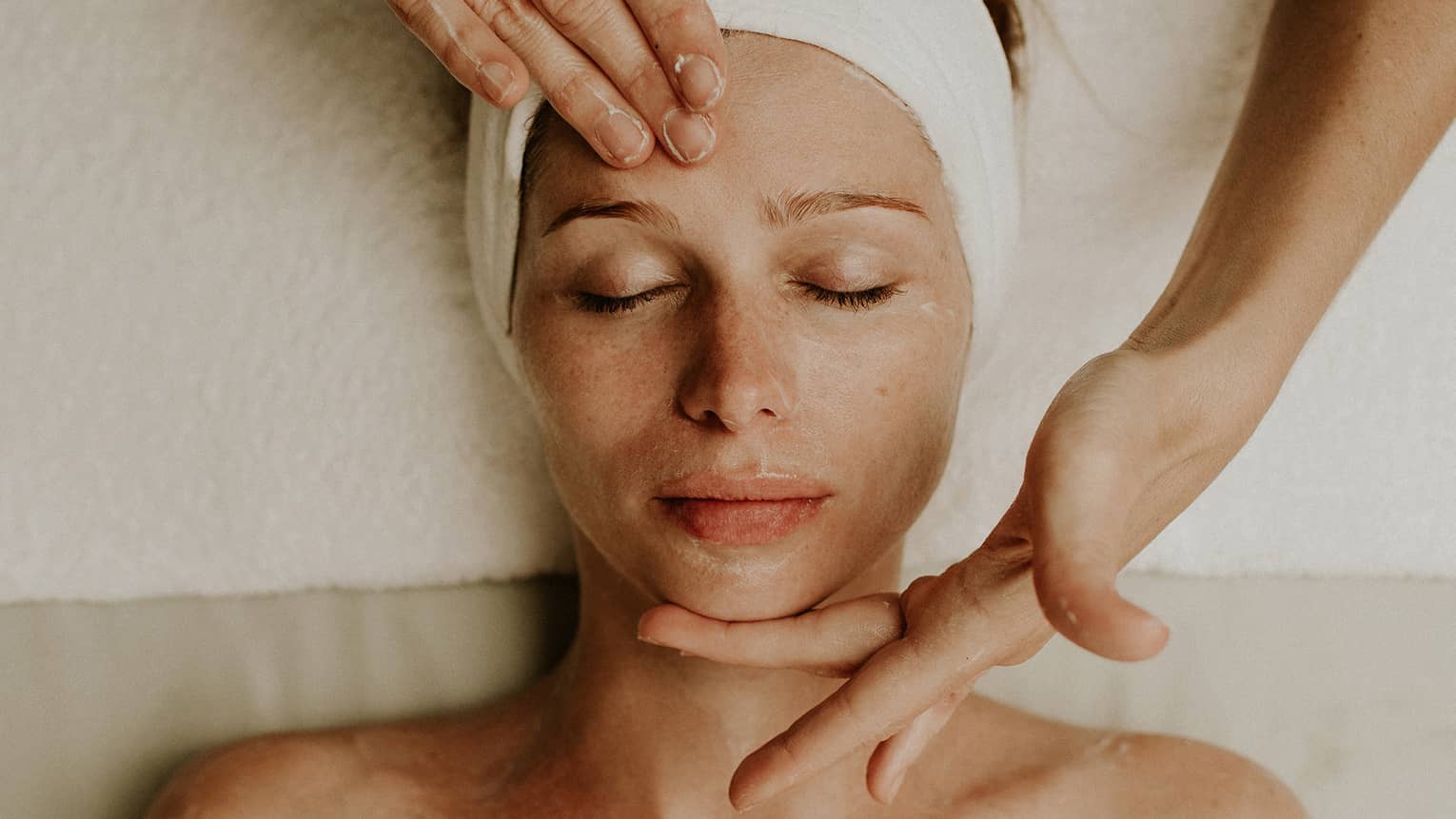 Person receiving a relaxing facial massage with eyes closed and head wrapped in a towel