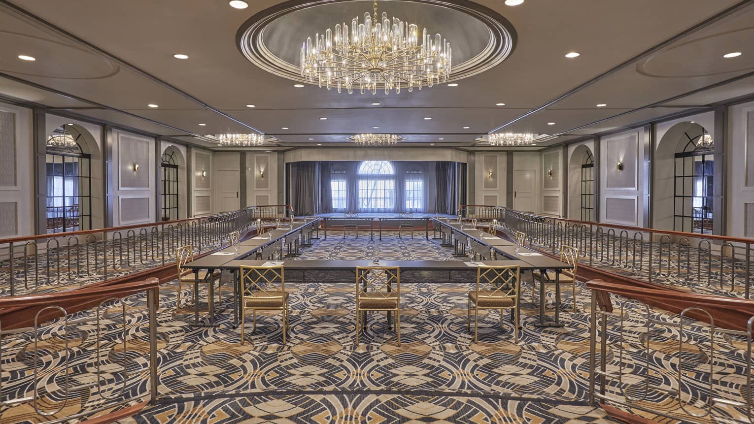 Large hotel ballroom with patterned blue, white and yellow carpet and a large crystal chandelier hanging in the centre
