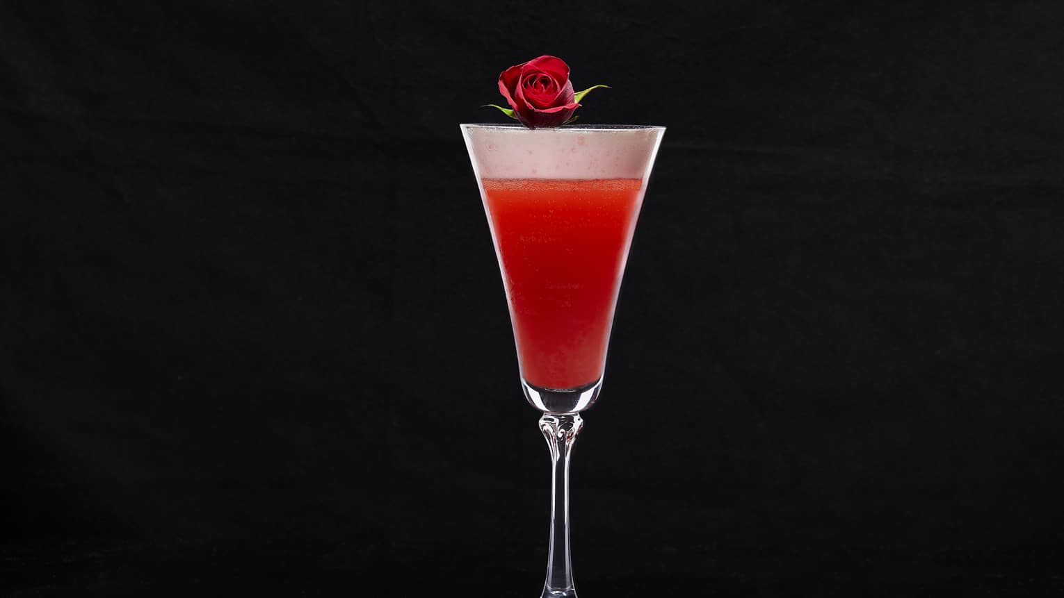Cocktail glass with red drink and a rose on top.