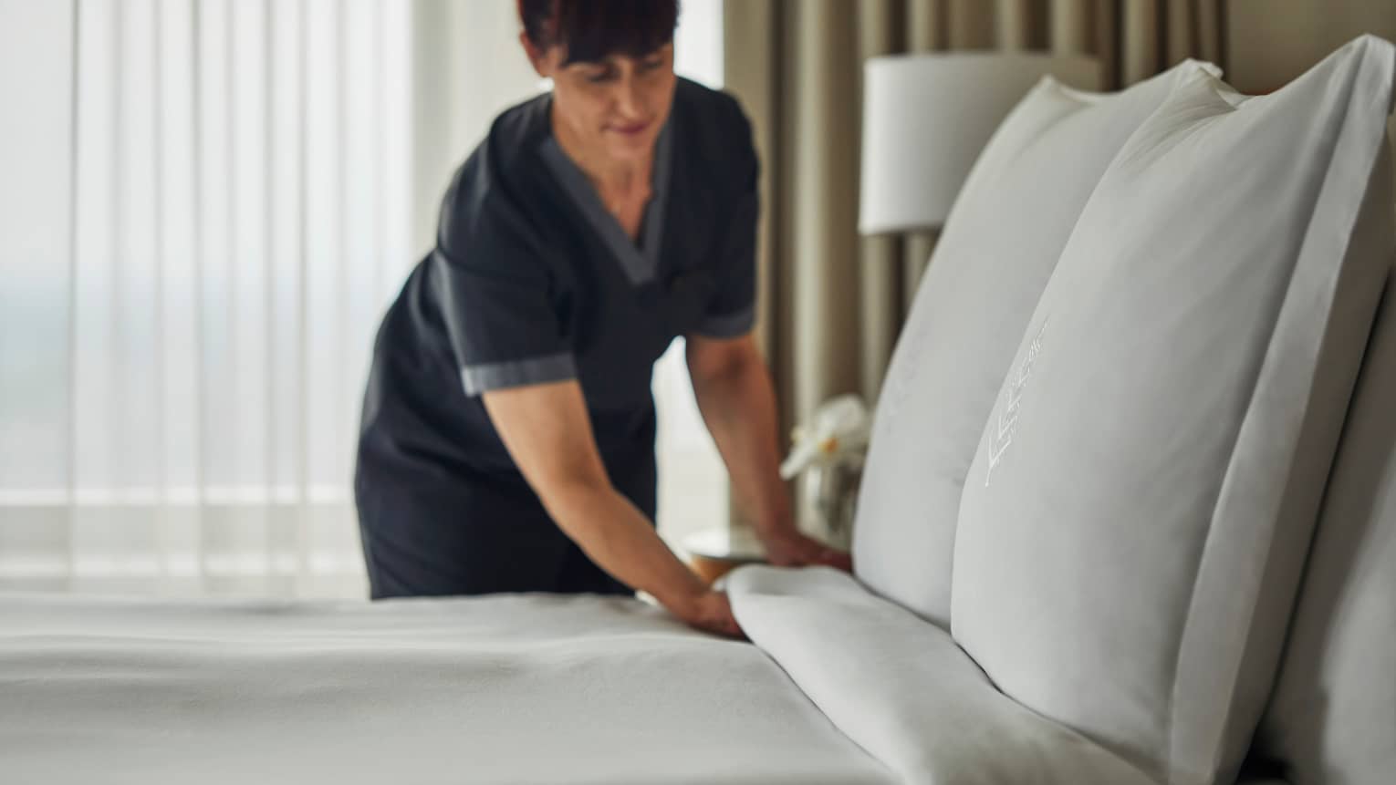 Hotel housekeeping staff makes bed, white linens and pillows