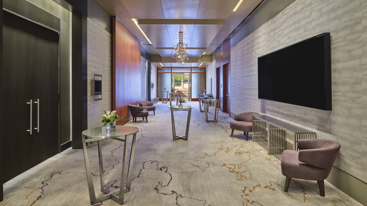 Hotel lobby pre-function space with contemporary round tables and seating vignette and large black TV on a wall opposite ballroom doors