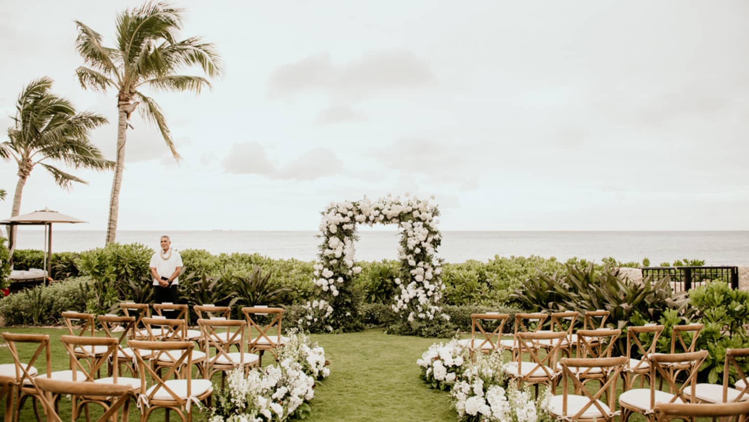 An outdoor wedding venue near the ocean, with wood chairs and flowers along a path.