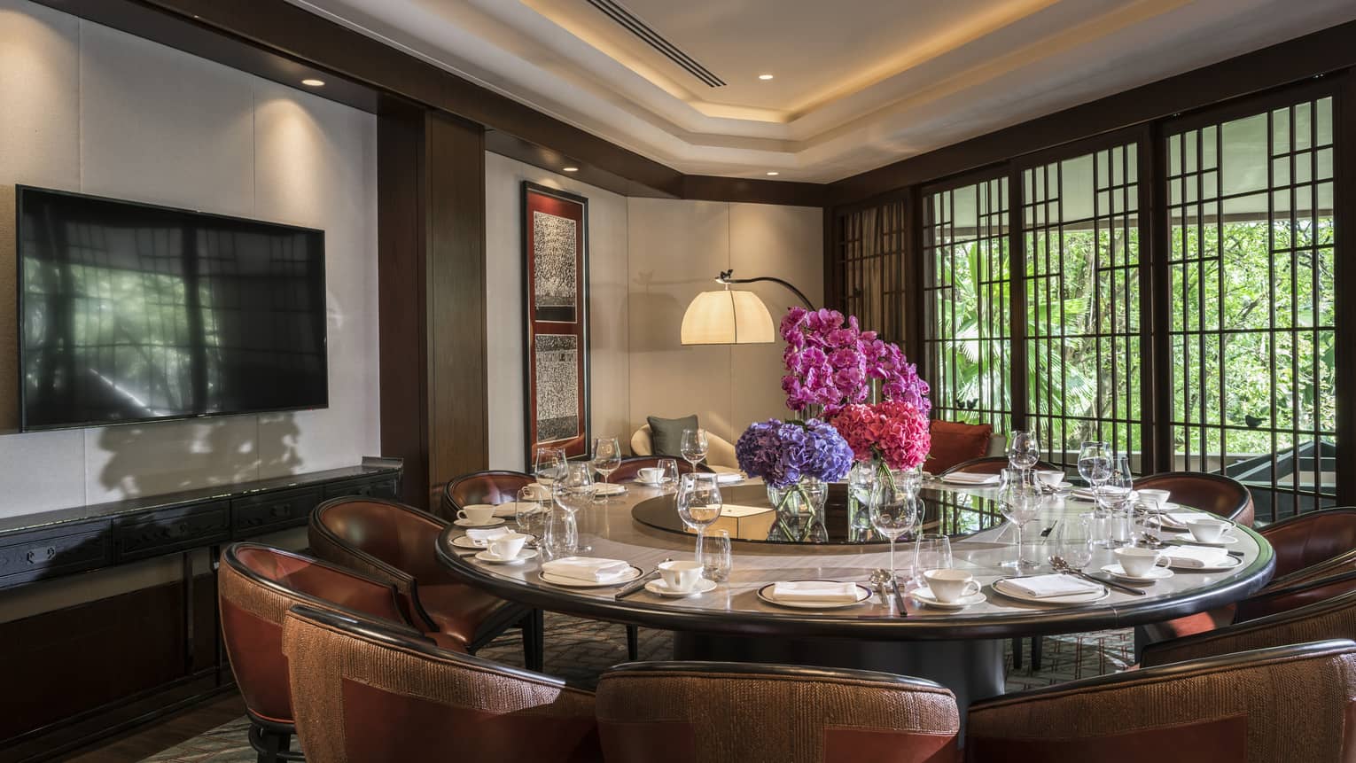 Round private dining meeting table with large pink floral display in centre, TV on wall