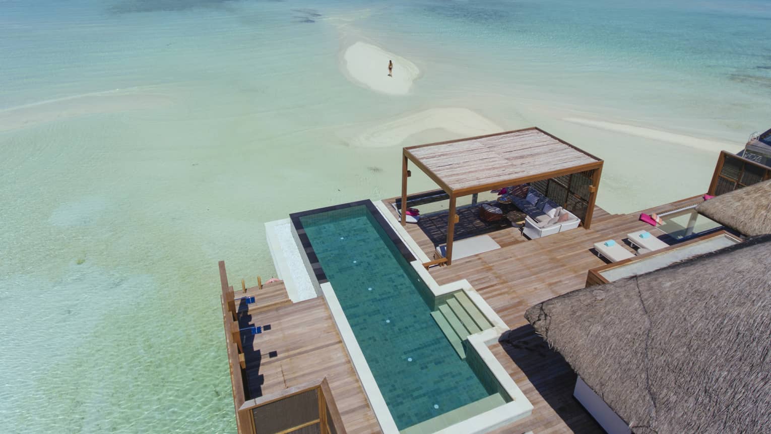 Aerial view of overwater bungalow with swimming pool, woman standing on sandbar in lagoon