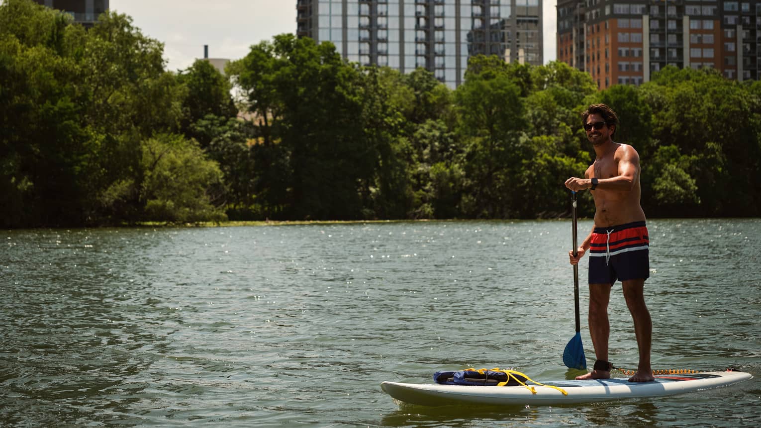 Person on a stand-up paddleboard in the water with trees and buildings in the background