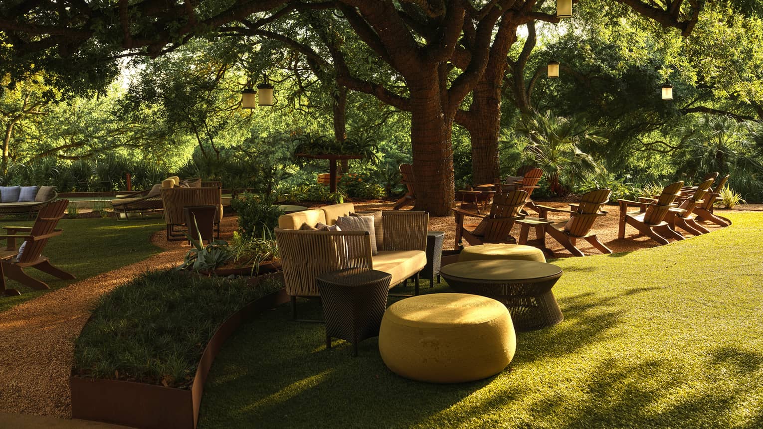 An outdoor sitting area below trees with couches and lawn chairs