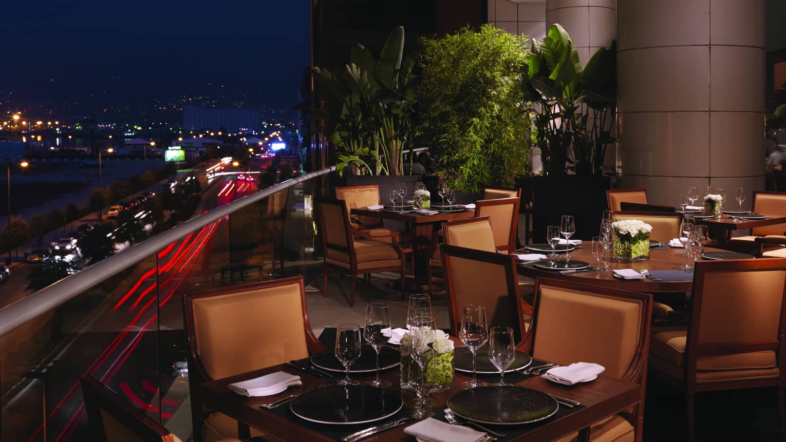 Sunny lobby lounge, hotel staff talk to guests at tables with white leather dining chairs, big gold and black vases behind