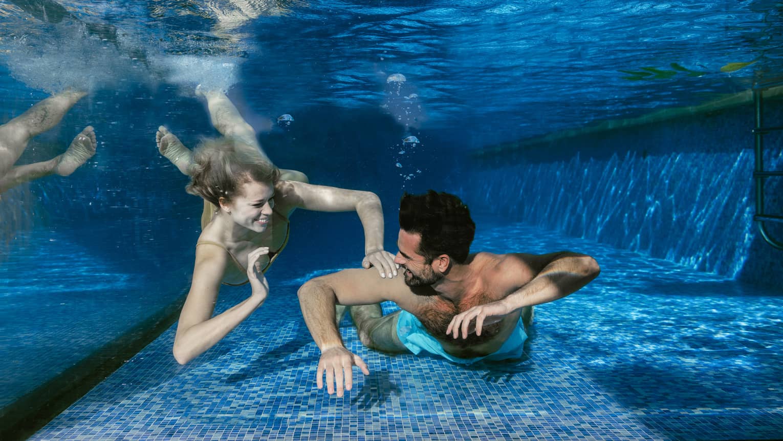 Two people swim underwater smiling at each other