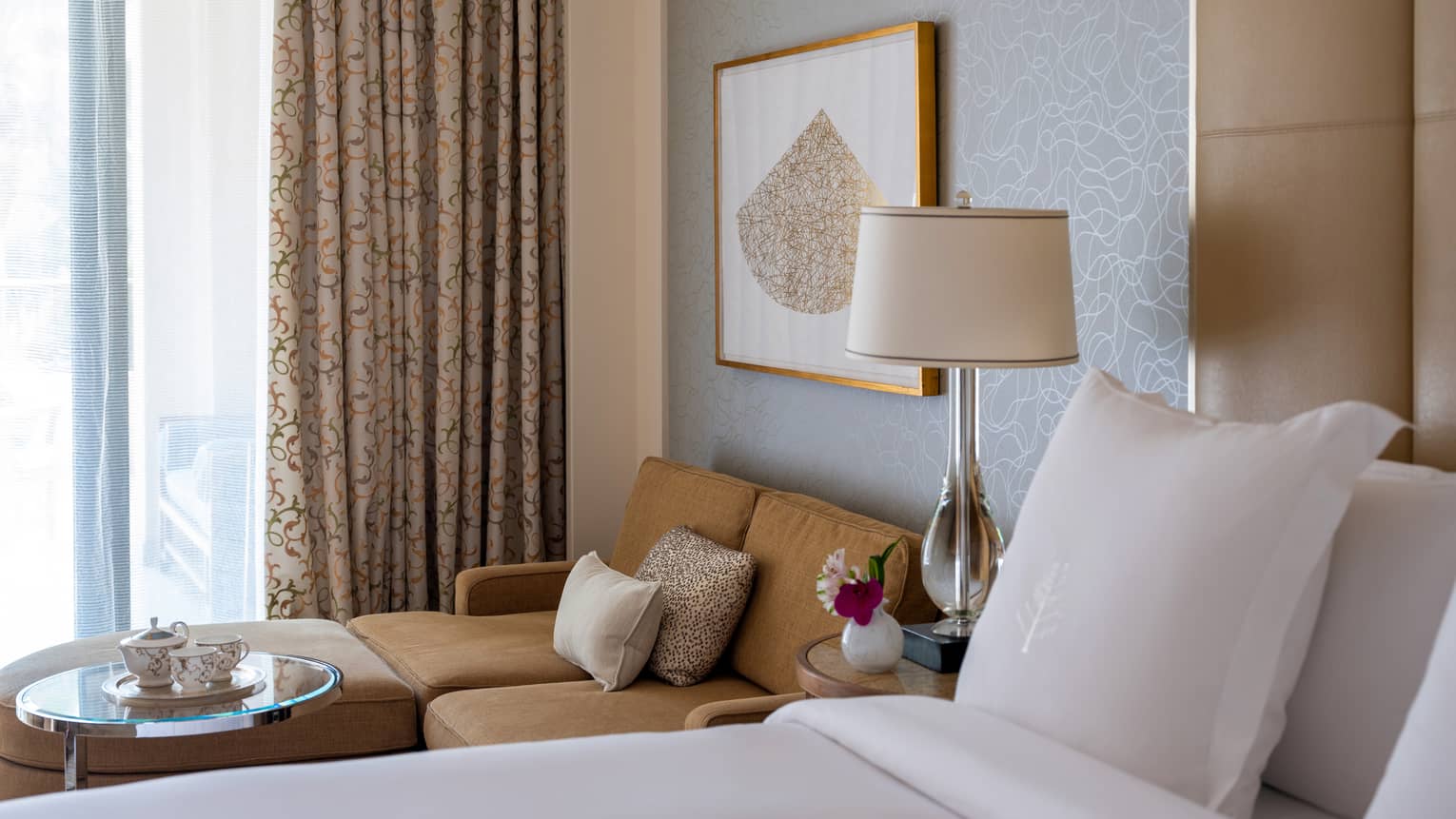 Bed next to a light brown sofa and glass coffee table, sliding glass doors