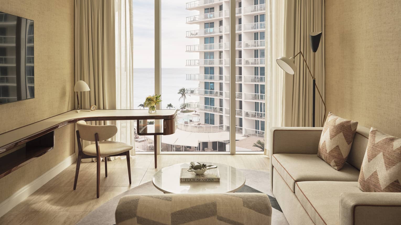Living area with sofa, desk and wall of windows with ocean view