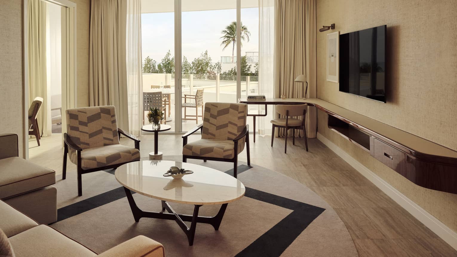 Living area with sofa, two arm chairs, desk, TV and walk-out balcony