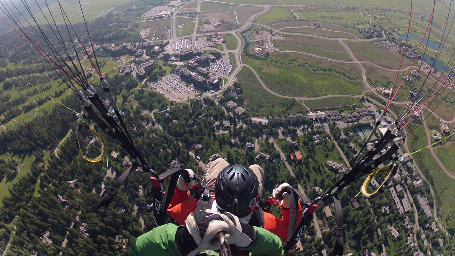 An aerial shot of a man paragliding, the lush greenery below rushing up to meet him 