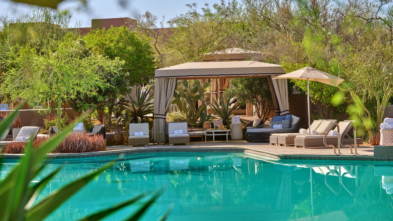 Blue pool with cabana and lounge chairs, surrounded by trees and greenery.