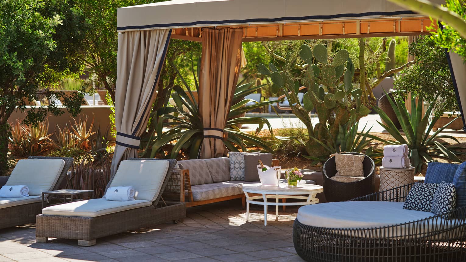 Cabana with lounge chairs, a couch, table and trees surrounding it.