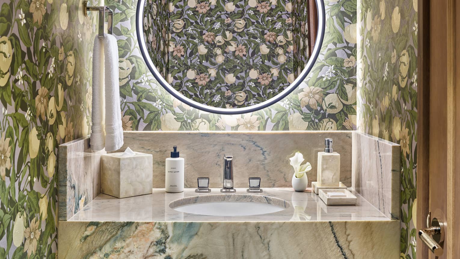 Bathroom with floral wall paper, illuminated round mirror, marble vanity