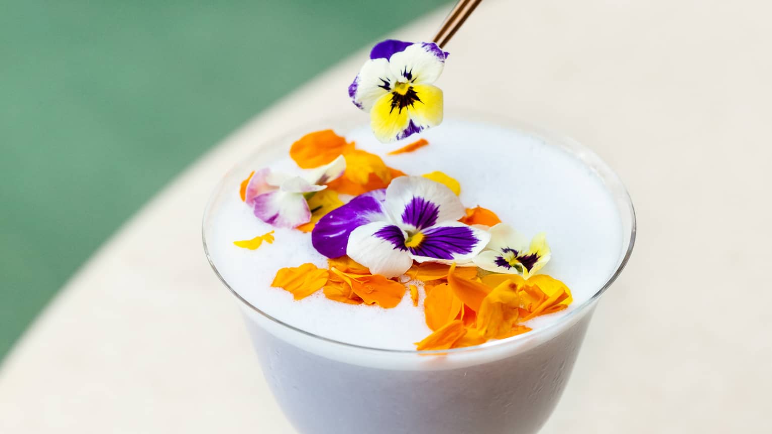 A stemmed glass of a white tropical cocktail topped with flowers