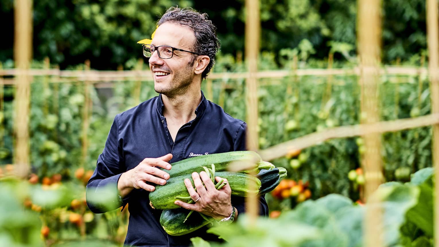 Chef holds large zucchinis in lush Kitchen Garden