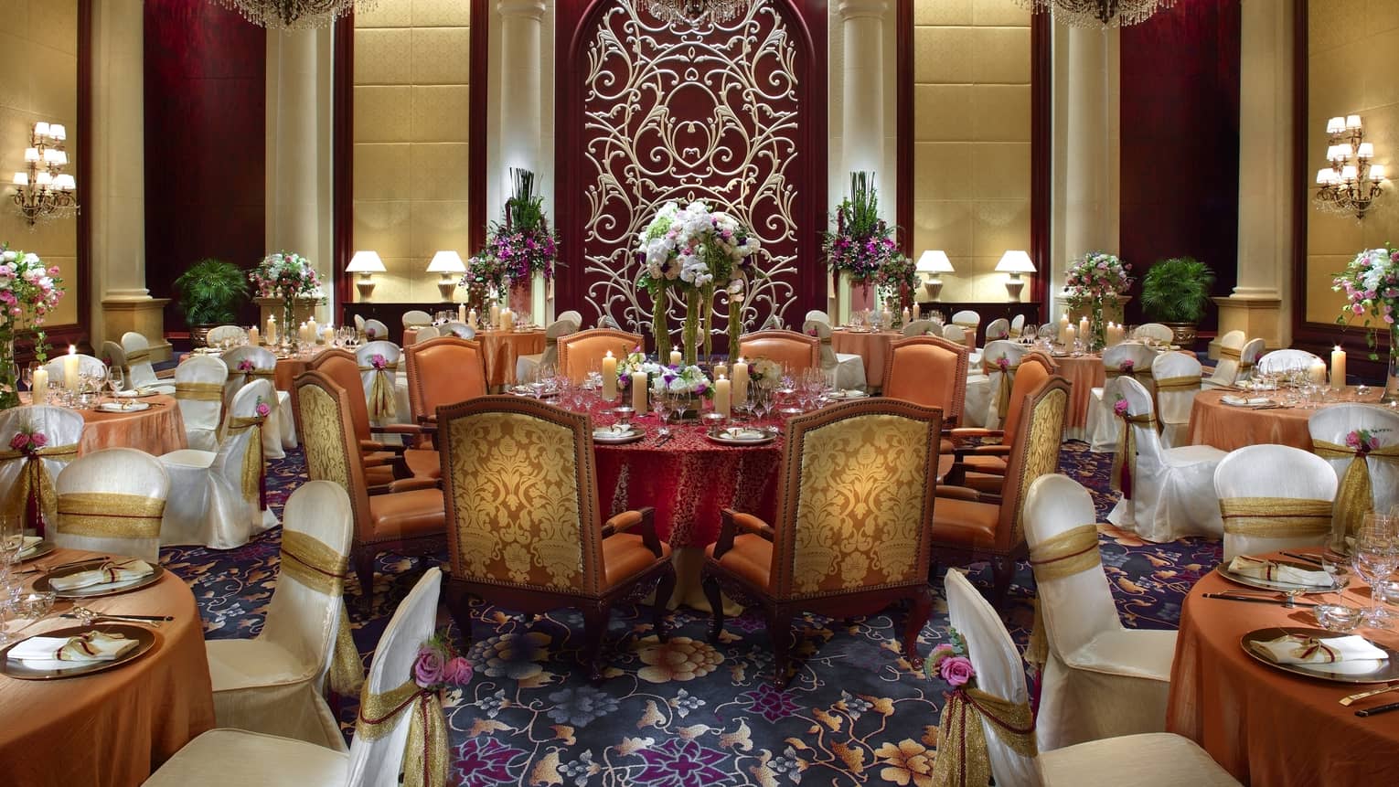 Opulent room decorated with candles, flowers, with round tables and plush chairs and carpet