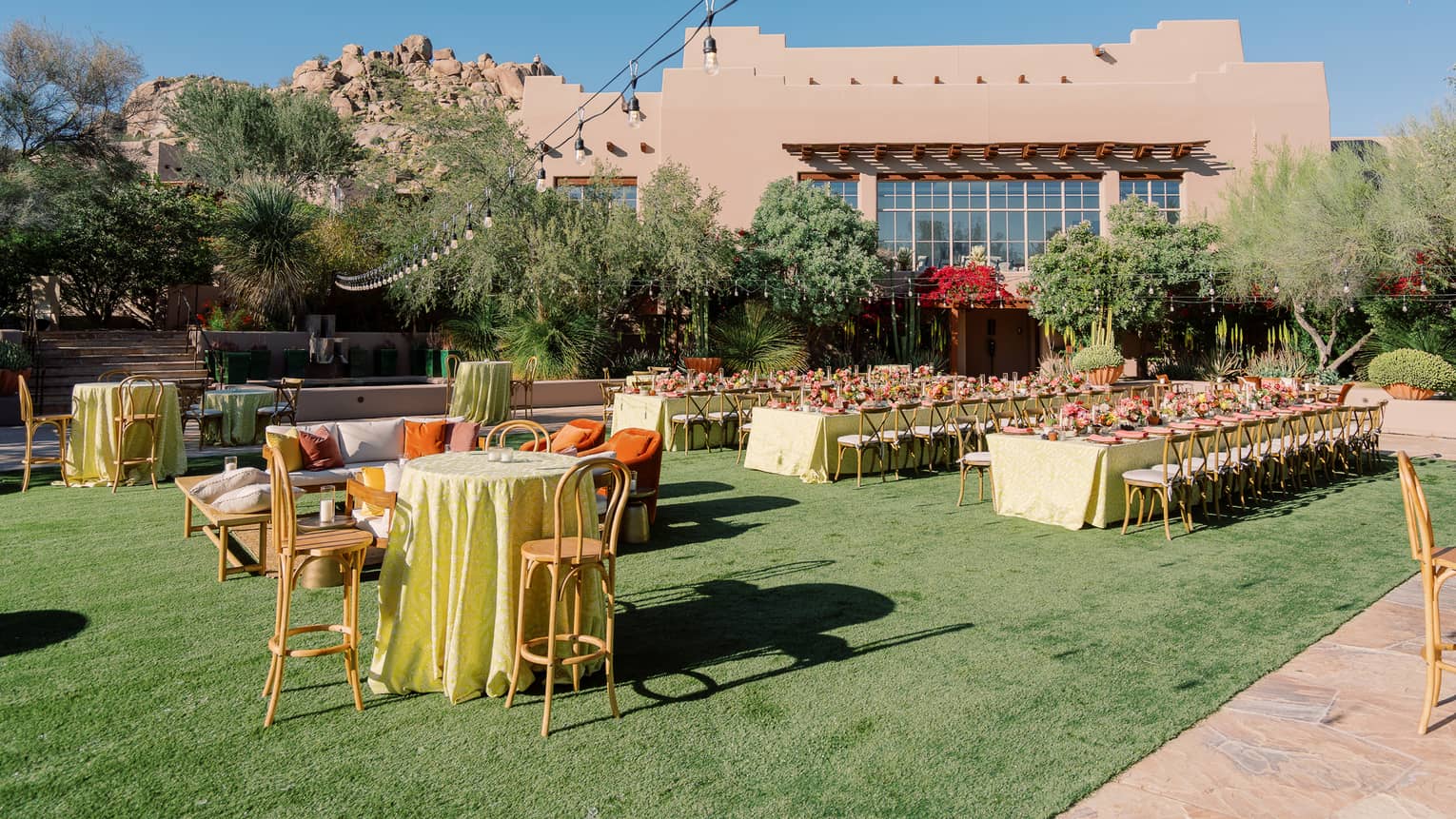 An outdoor venue with tables and chairs with place settings and a string of lights above