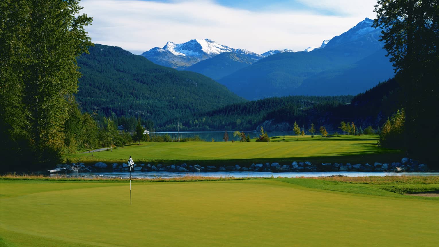 Big Sky Golf Course green, flag in front of pond, snow-capped mountains in background
