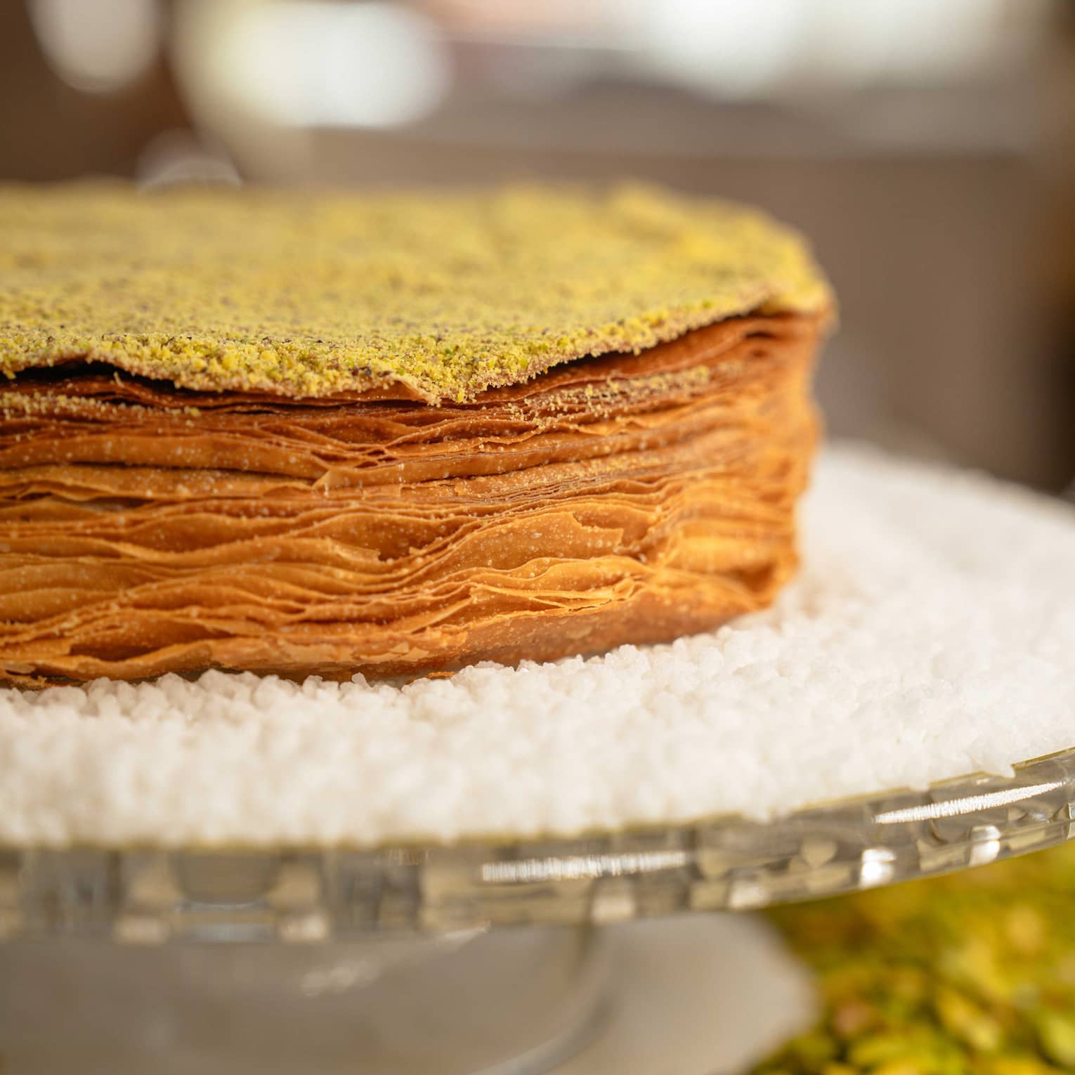 Close up of multi-layered pastry cake surrounded by white powdered sugar on a glass cakestand