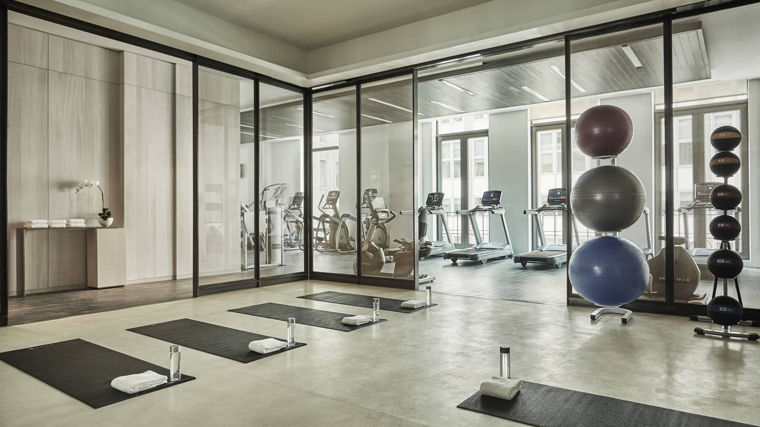 Yoga mats and water bottles in rows on Fitness Centre flow, stack of pilates balls