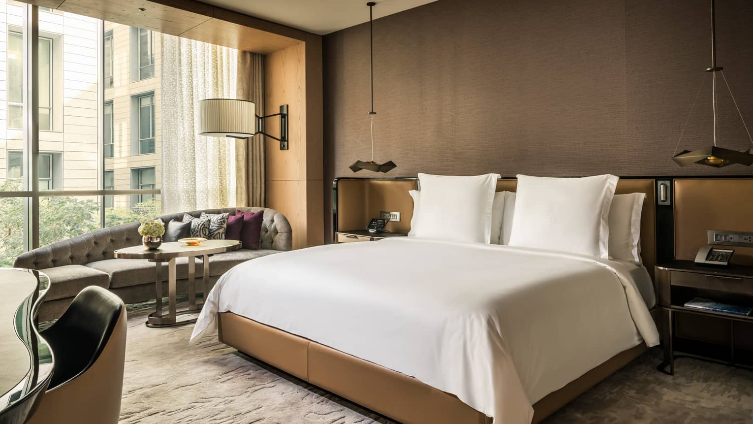 Deluxe Room hotel bed with padded headboard and nightstands, chaise under sunny window