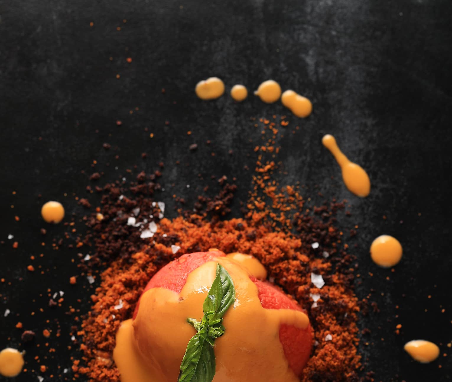 A close up of a orange sorbet like dish covered in an orange sauce and garnished with mint 