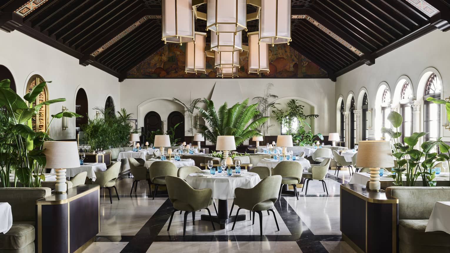 Light-filled restaurant with white walls, windows, dark wooden beams on pitched ceiling, hanging lantern-style lights