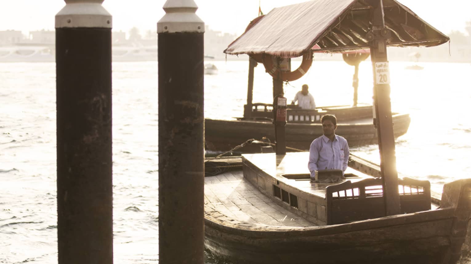 Two men in covered wood boats on Dubai Creek water by dock