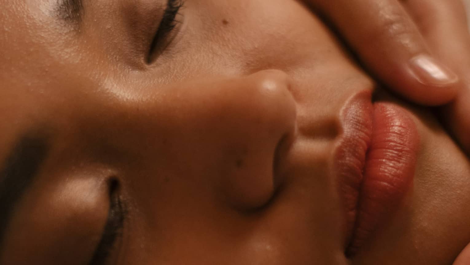 Closeup of hands on either side of woman’s face during facial