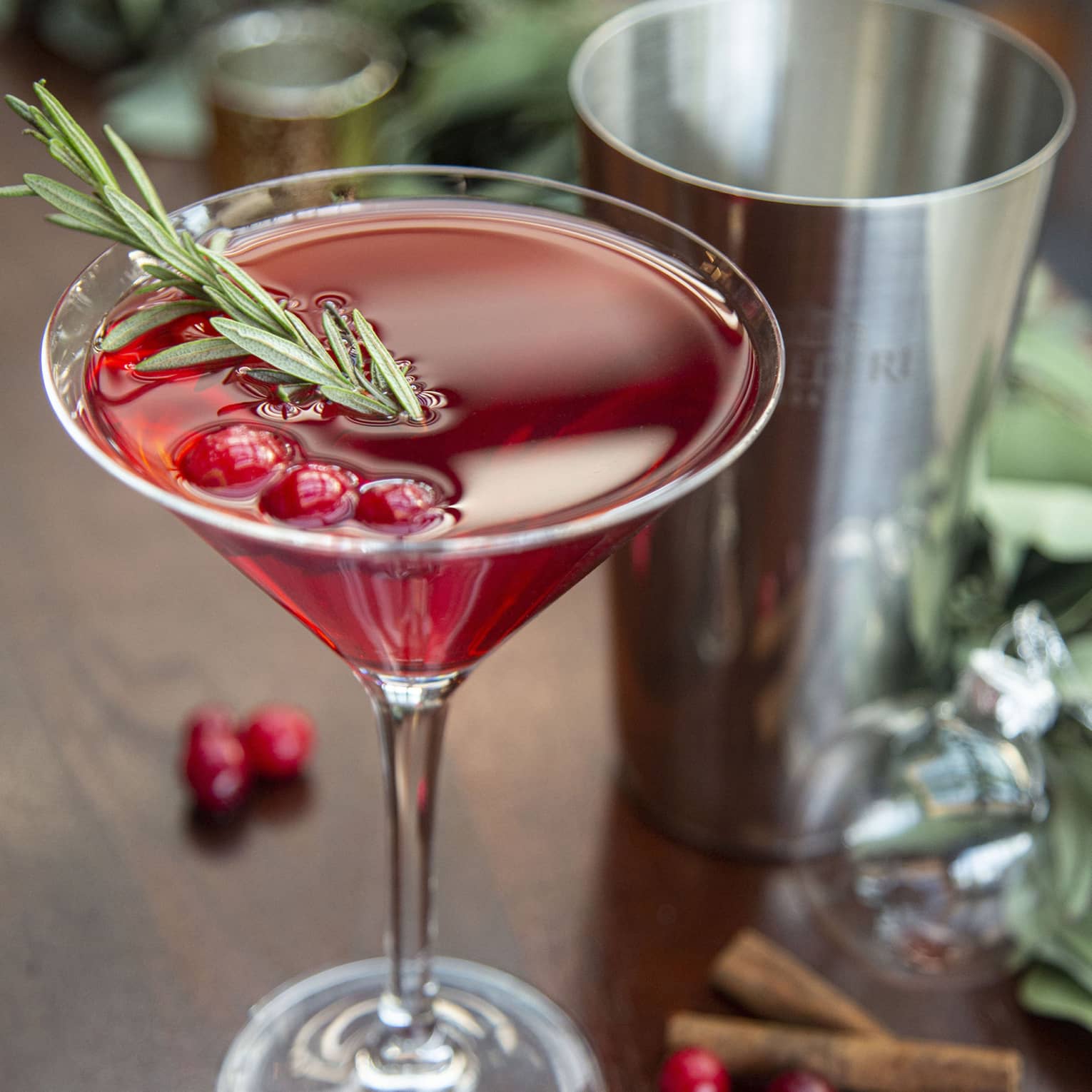 Berry Merry Martini, a red cocktail with rosemary sprig and cranberries