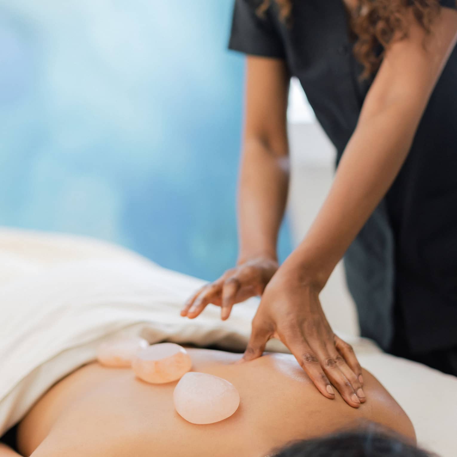 Masseuse places salt stones on a person's bare back