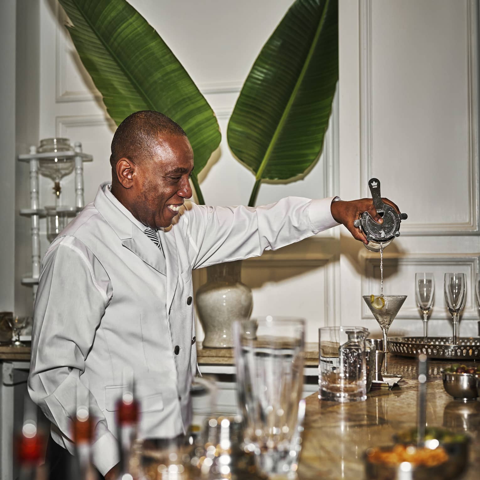 Bartender wearing a white double-breasted coat pours a cocktail into a martini glass